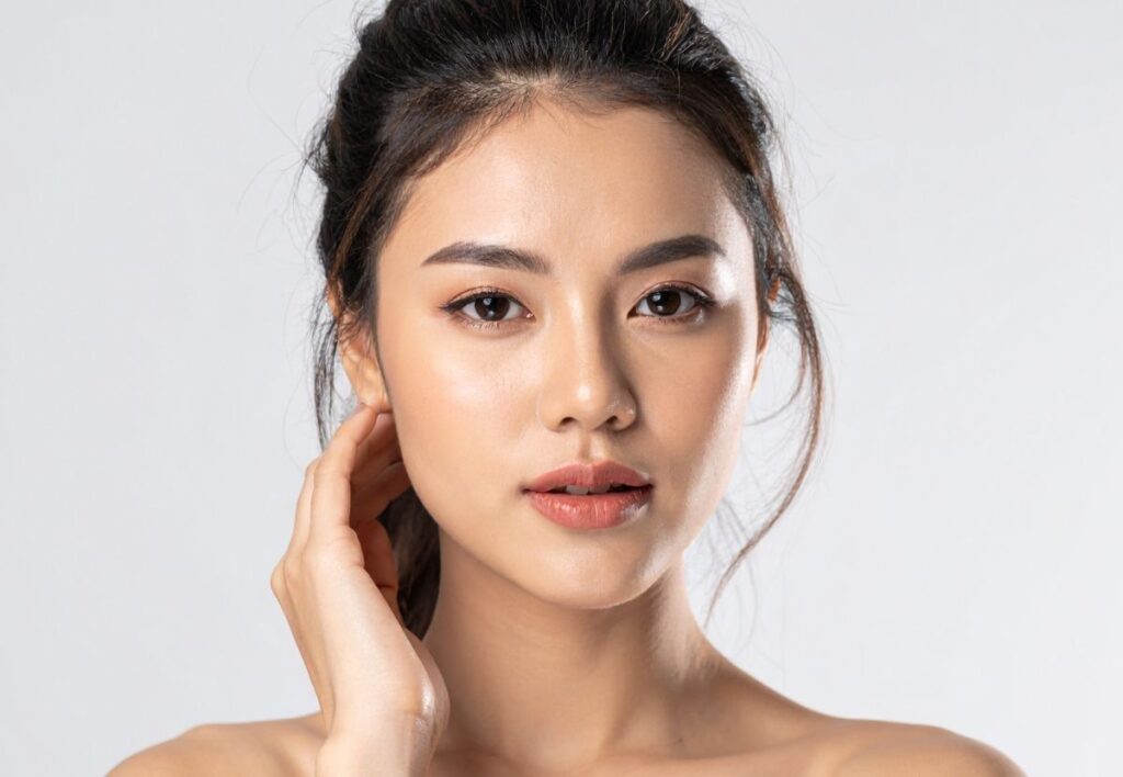 Asian woman with smooth, balanced facial contours after facial fat transfer at Aestira in Miami.